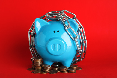Photo of Piggy bank  with steel chain and coins on red background. Money safety concept