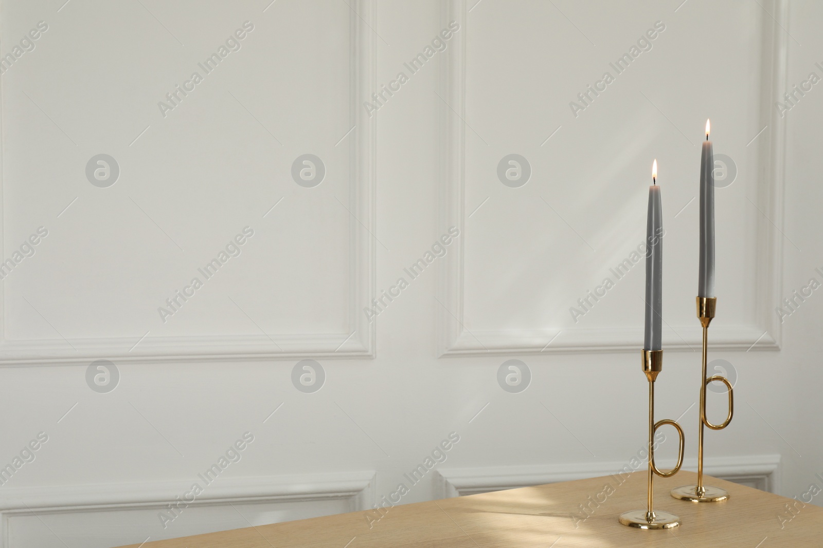 Photo of Holders with burning candles on wooden table near white wall indoors, space for text