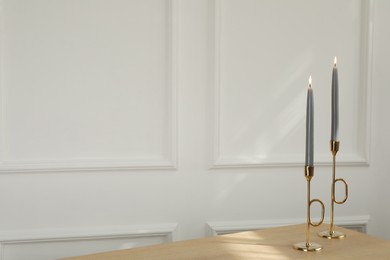 Photo of Holders with burning candles on wooden table near white wall indoors, space for text