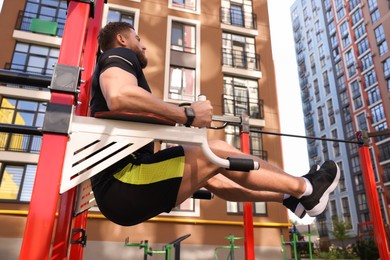 Man doing leg rise exercise at outdoor gym, low angle view