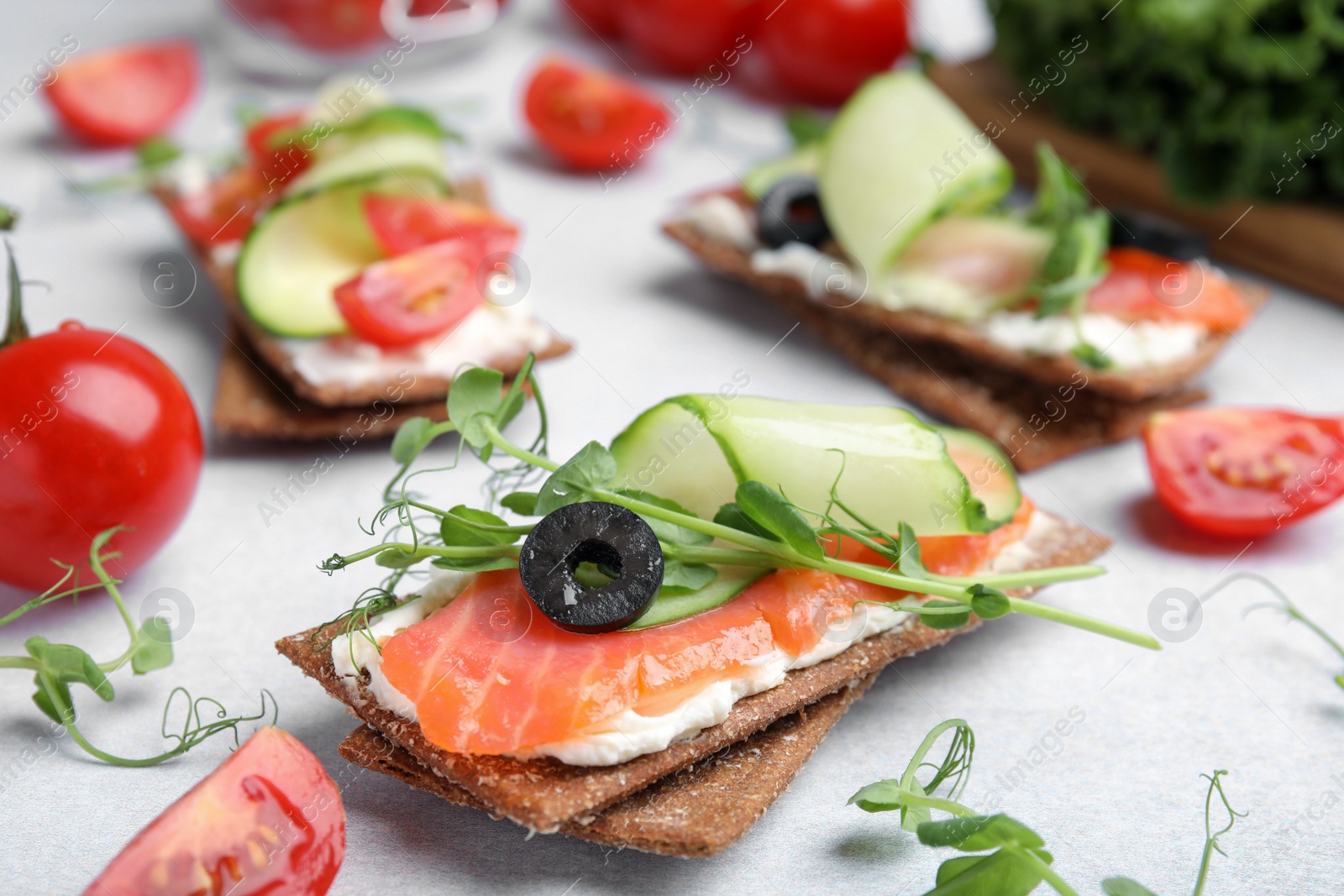 Photo of Tasty rye crispbreads with salmon, cream cheese and cucumber on light grey table, closeup