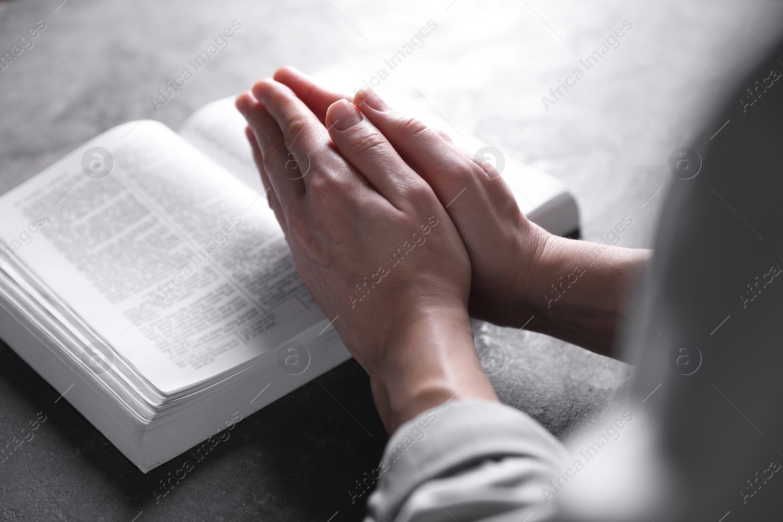 Photo of Religion. Christian woman praying over Bible at gray table, closeup