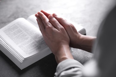 Photo of Religion. Christian woman praying over Bible at gray table, closeup