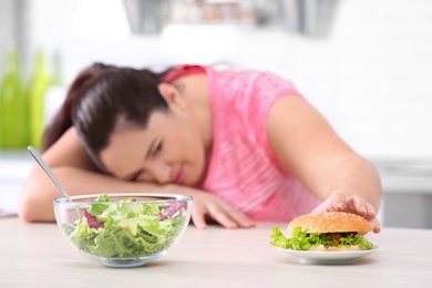 Salad and burger with blurred overweight woman on background. Healthy diet