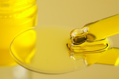 Photo of Dripping face serum from pipette on yellow background, closeup