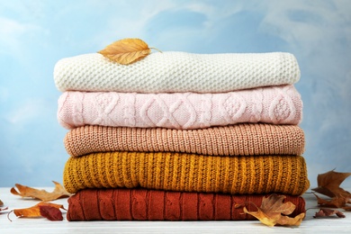 Photo of Stack of warm clothes and autumn leaves on white wooden table against light blue background