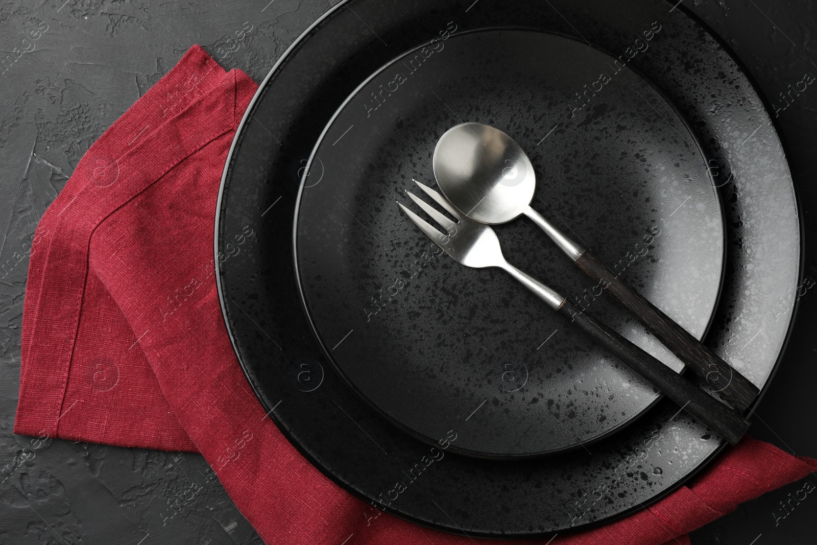 Photo of Stylish setting with cutlery, napkin and plates on dark textured table, top view