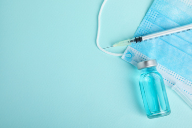 Photo of Vial, syringe and surgical mask on turquoise  background, flat lay with space for text. Vaccination and immunization