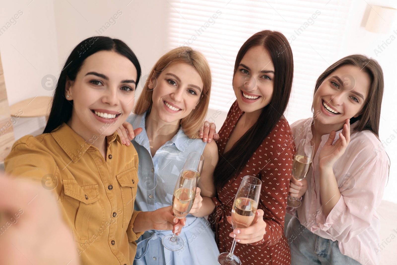 Photo of Beautiful young ladies with champagne taking selfie at home. Women's Day