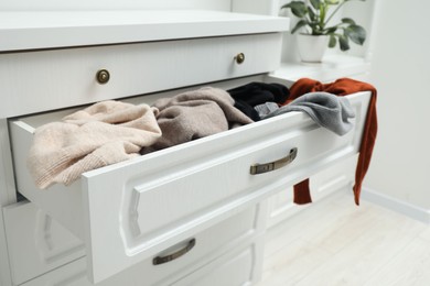 Photo of Cluttered chest of drawers indoors. Clothes in mess