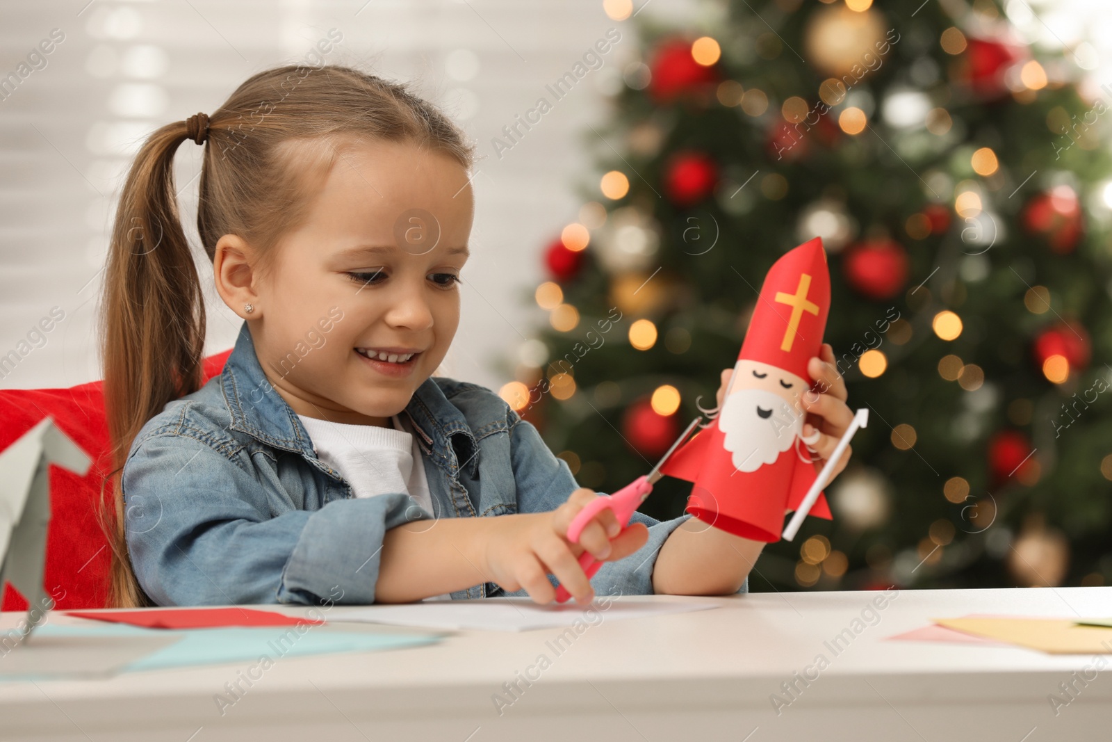 Photo of Cute little girl making paper Saint Nicholas toy at home