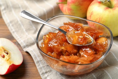Photo of Tasty apple jam in glass bowl and fresh fruits on table, closeup
