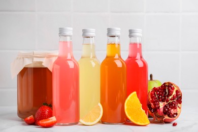 Delicious kombucha in glass bottles, jar and fresh fruits on white marble table