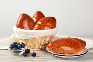 Photo of Delicious baked pirozhki and blueberries on wooden table