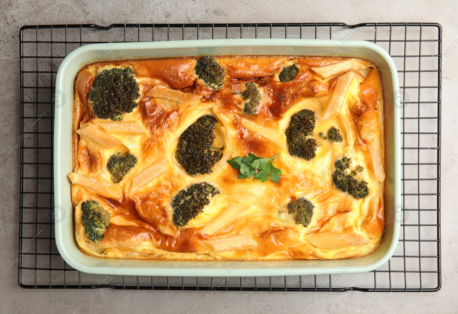 Photo of Tasty broccoli casserole in baking dish on cooling rack, top view