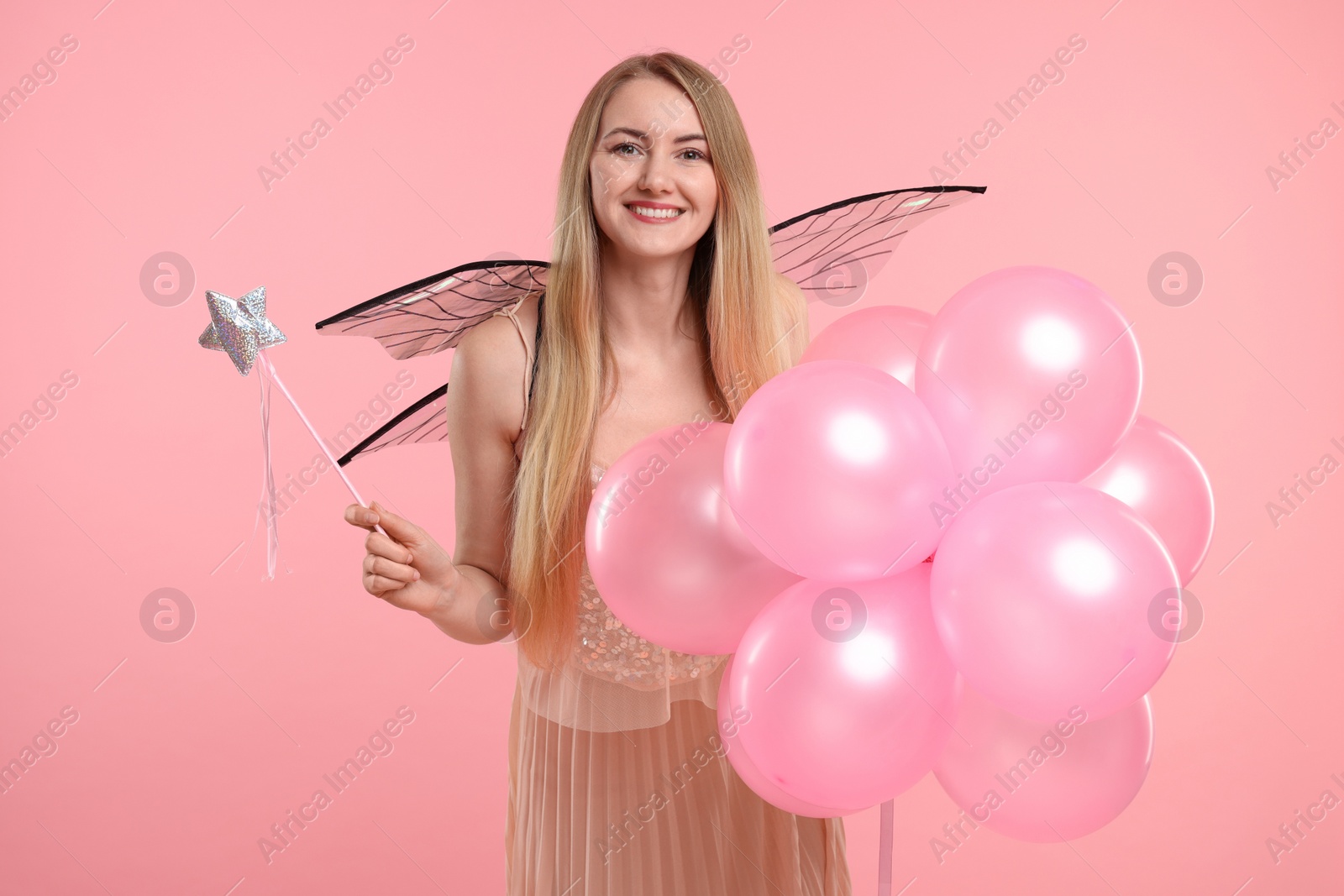 Photo of Beautiful girl in fairy costume with wings, magic wand and balloons on pink background