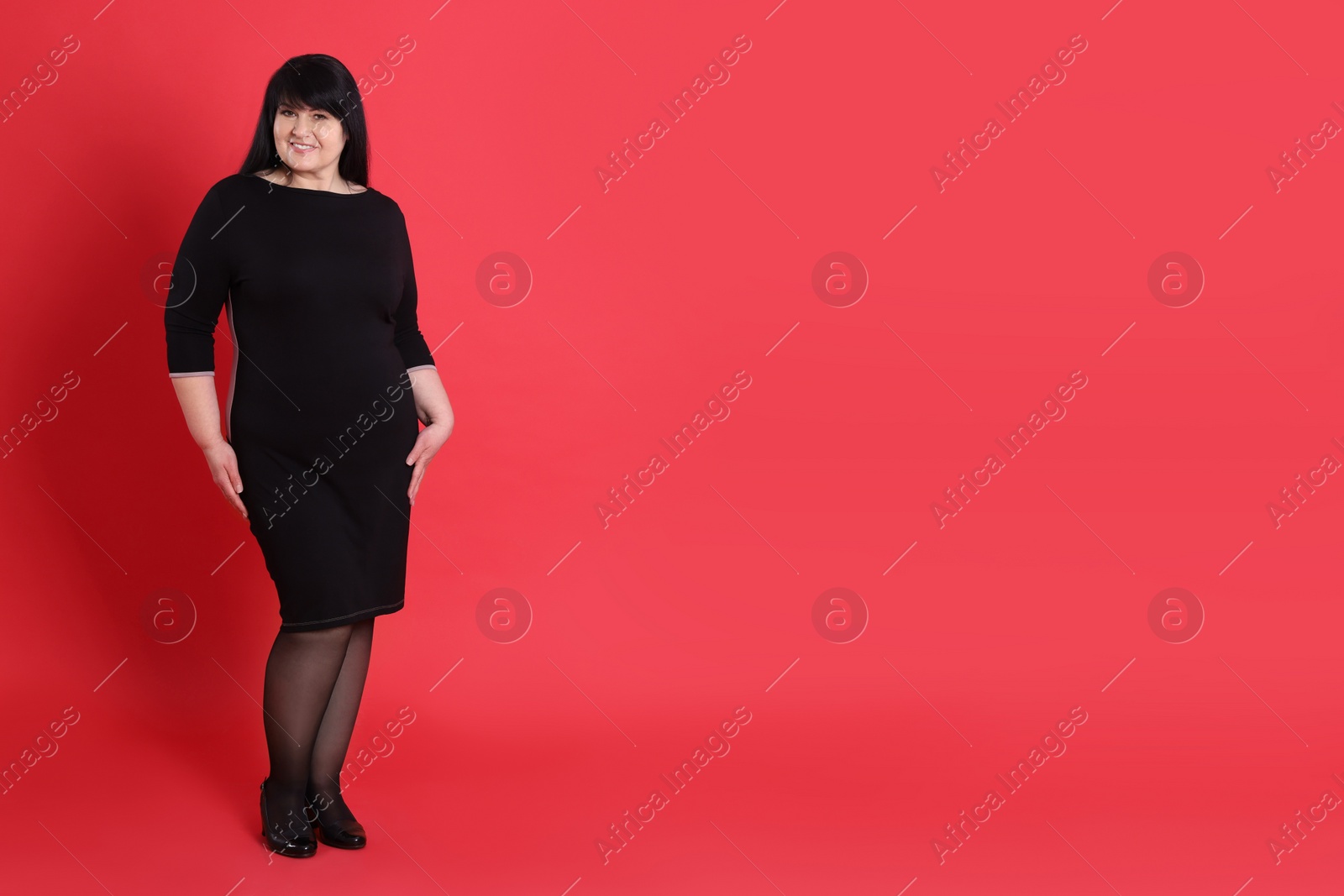Photo of Beautiful overweight woman in black dress on red background. Space for text