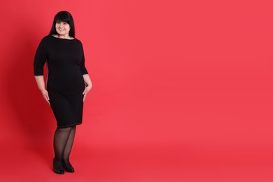 Beautiful overweight woman in black dress on red background. Space for text