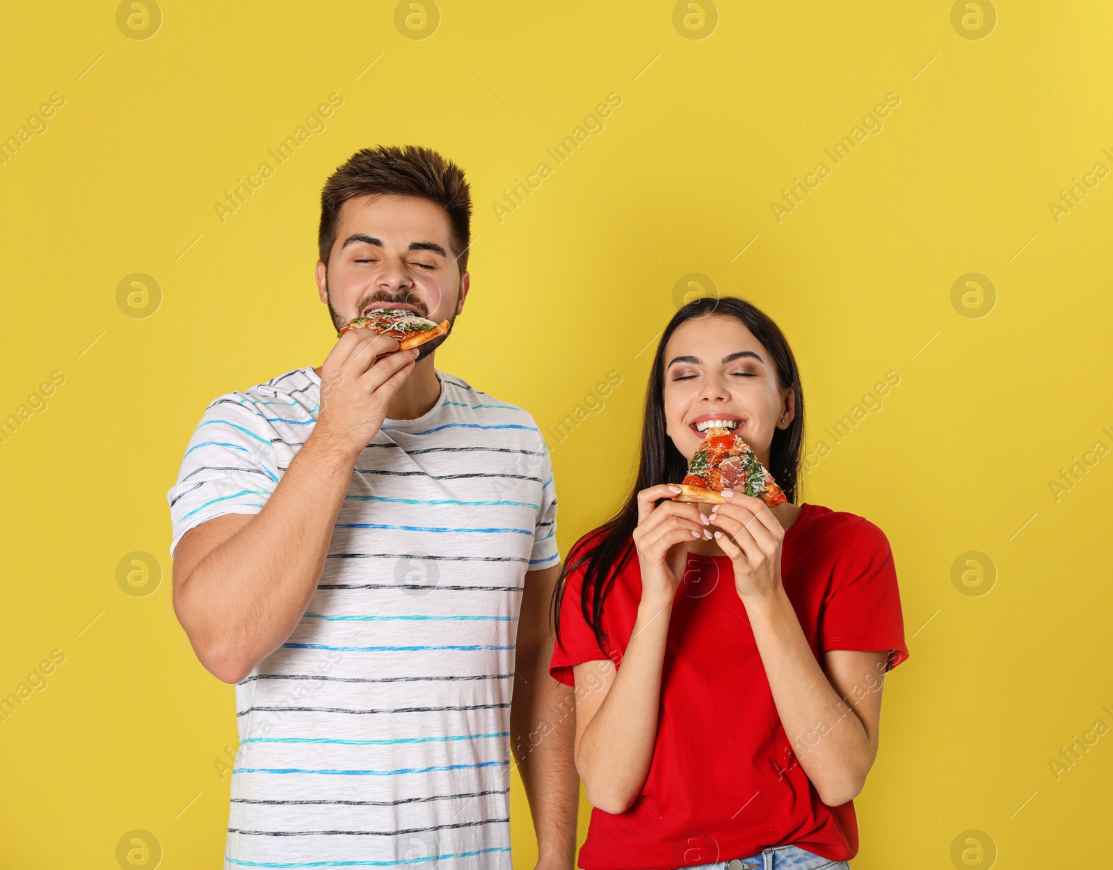 Photo of Young couple eating pizza on yellow background