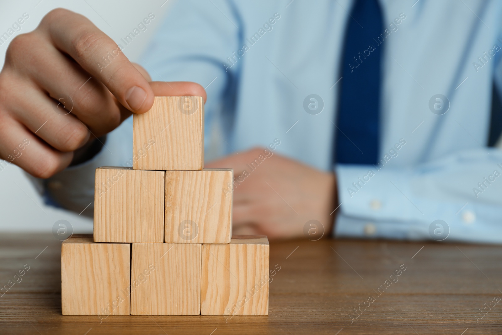 Photo of Businessman building pyramid of blank cubes on wooden table, closeup. Space for text