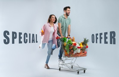 Image of Special offer. Young couple with shopping cart fullgroceries on grey background