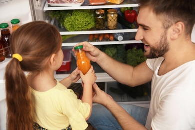 Photo of Young father with daughter taking juice from refrigerator at home