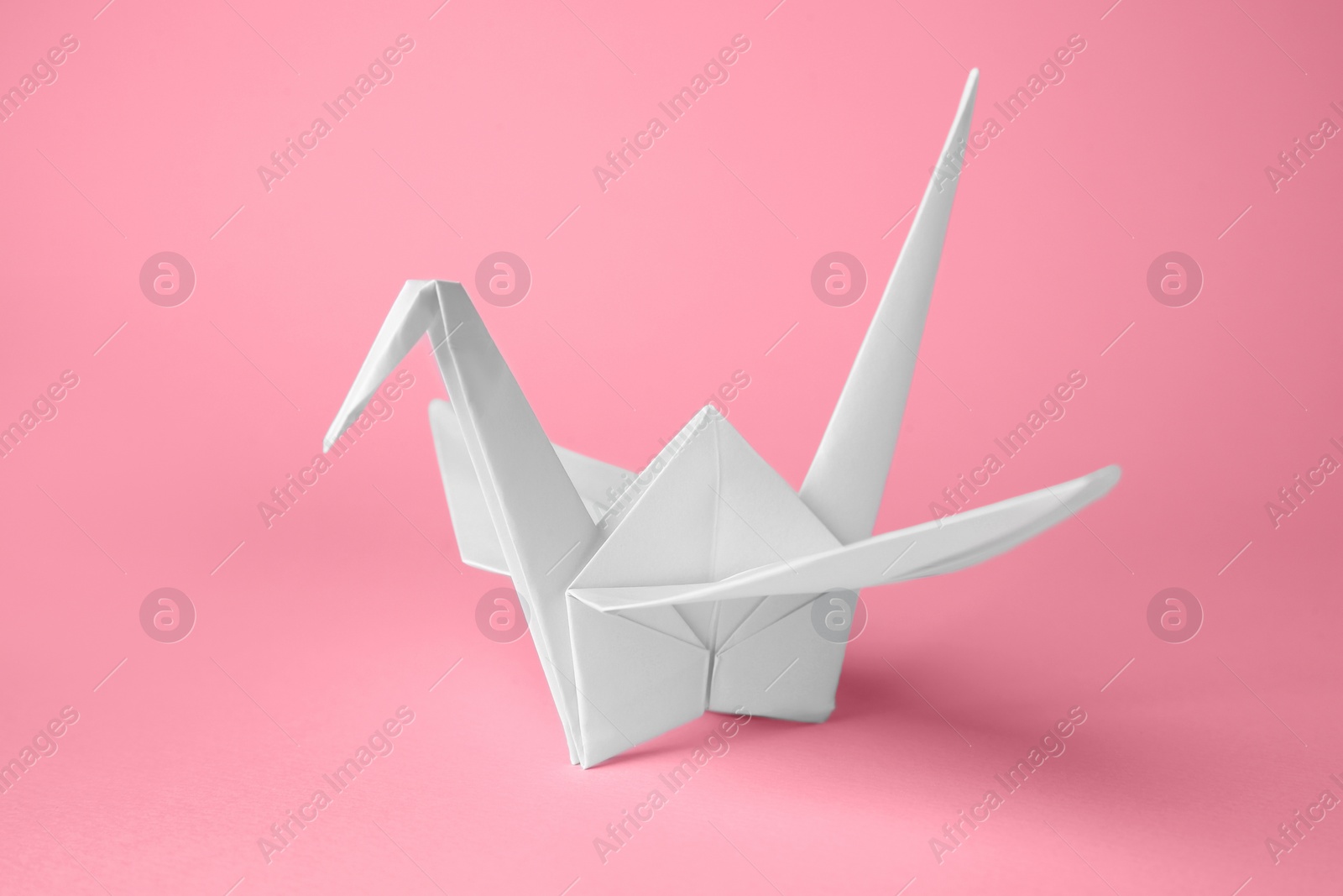 Photo of Origami art. Handmade paper crane on pink background, closeup