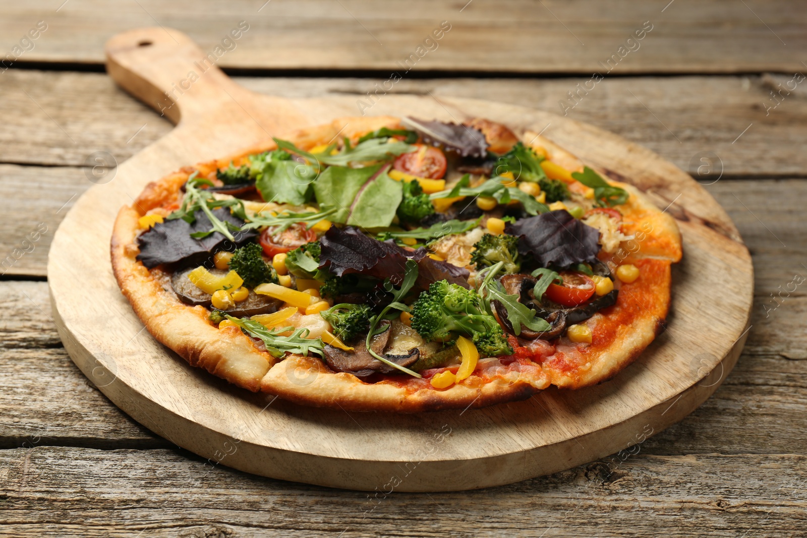 Photo of Delicious vegetarian pizza with mushrooms, vegetables and greens on wooden table