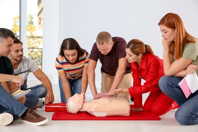 Photo of Group of people with instructor practicing CPR on mannequin at first aid class indoors