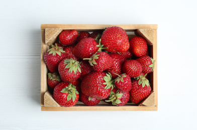 Photo of Delicious ripe strawberries in crate on white wooden table, top view