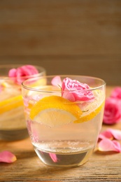 Photo of Tasty refreshing lemon drink with roses on wooden table