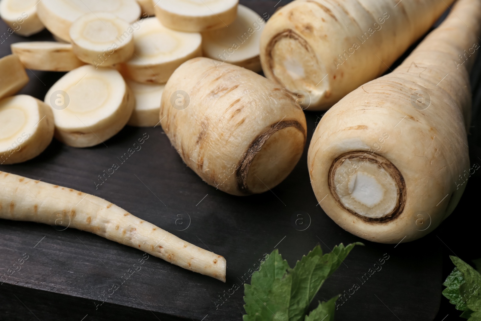 Photo of Whole and cut parsnips on wooden board, closeup