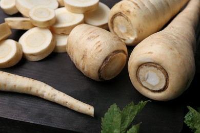 Whole and cut parsnips on wooden board, closeup