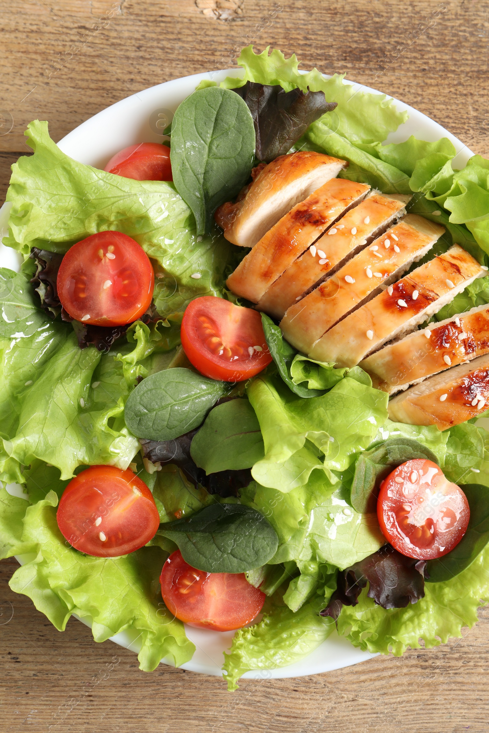 Photo of Delicious salad with chicken, cherry tomato and spinach on wooden table, top view