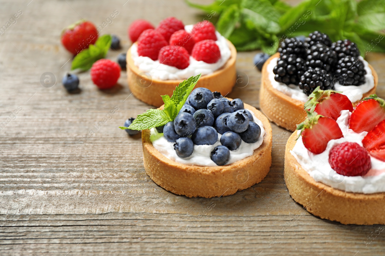 Photo of Different berry tarts on wooden table. Delicious pastries