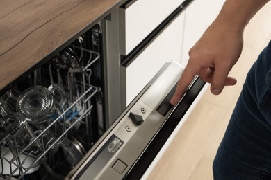 Photo of Man pushing button on dishwasher's door indoors, closeup