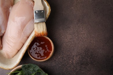 Photo of Marinade, basting brush and raw chicken fillets on brown table, flat lay. Space for text