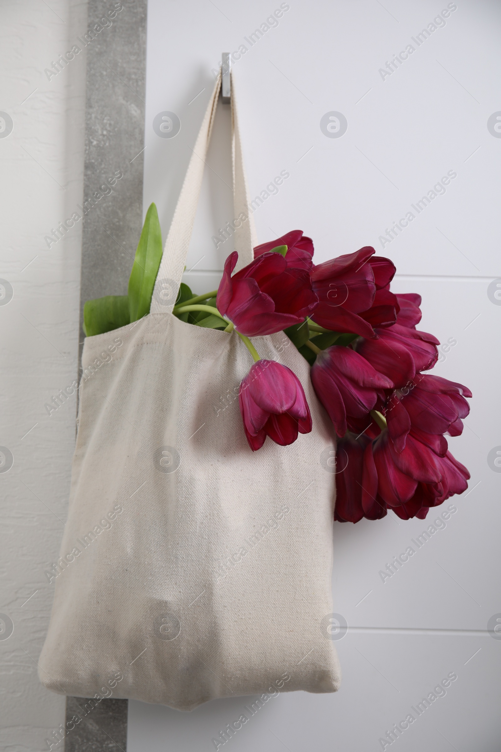 Photo of Tote bag with beautiful purple tulips hanging on white wall indoors
