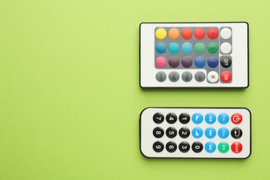 Remote controls on light green background, flat lay. Space for text