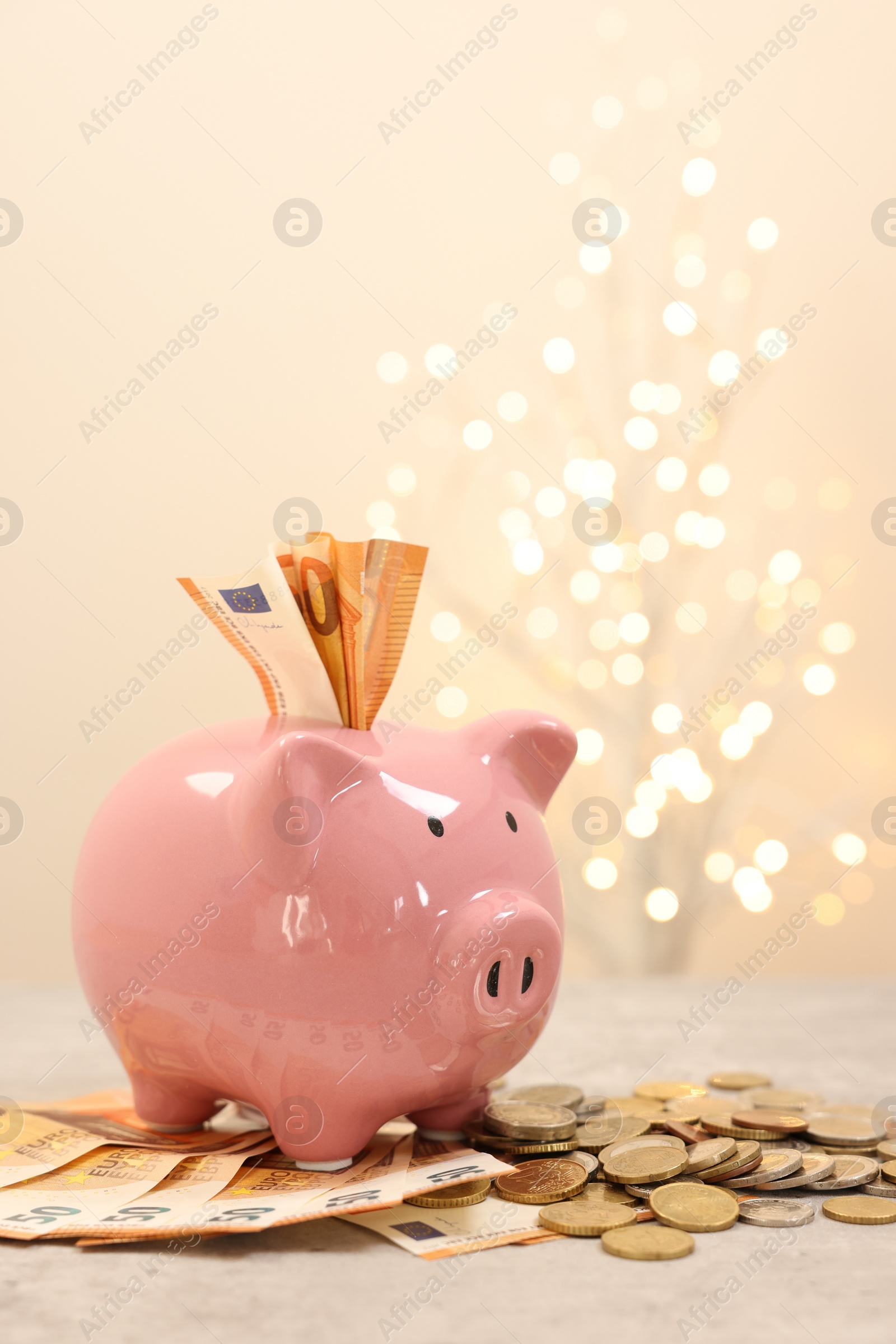 Photo of Piggy bank with euro banknotes and coins on grey table against blurred lights, space for text