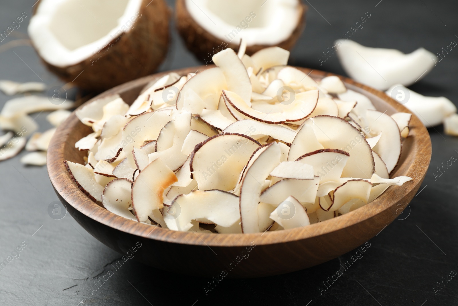 Photo of Tasty coconut chips in bowl on black table