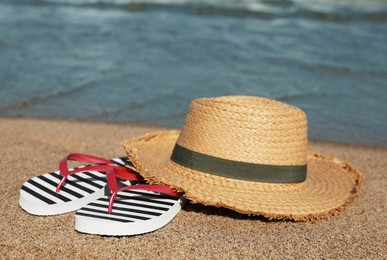 Striped flip flops and straw hat on sandy beach near sea