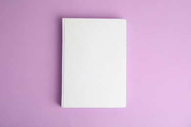 Book with blank cover on violet background, top view