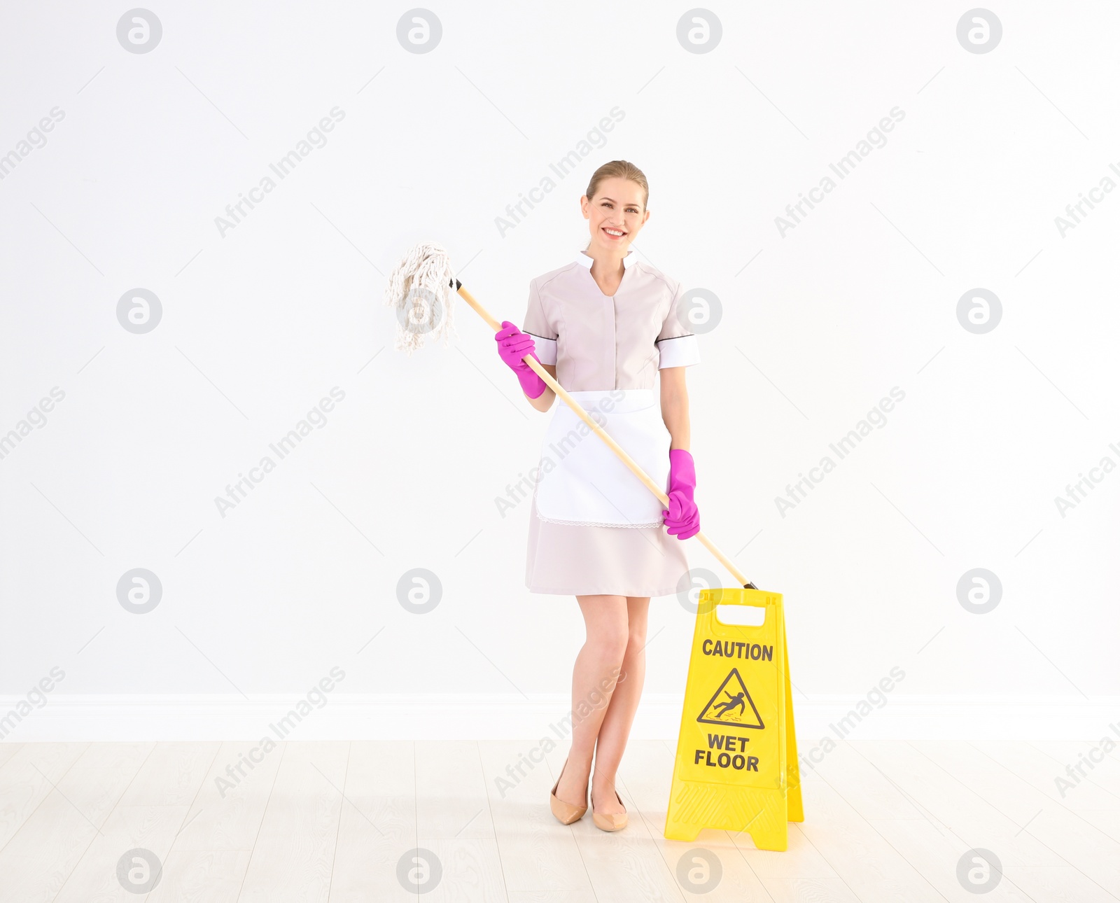 Photo of Young chambermaid with mop near WET FLOOR sign indoors