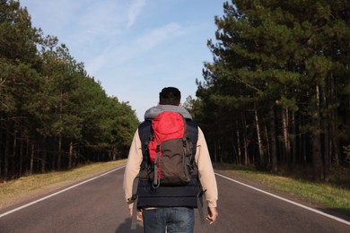 Man with backpack on road near forest, back view