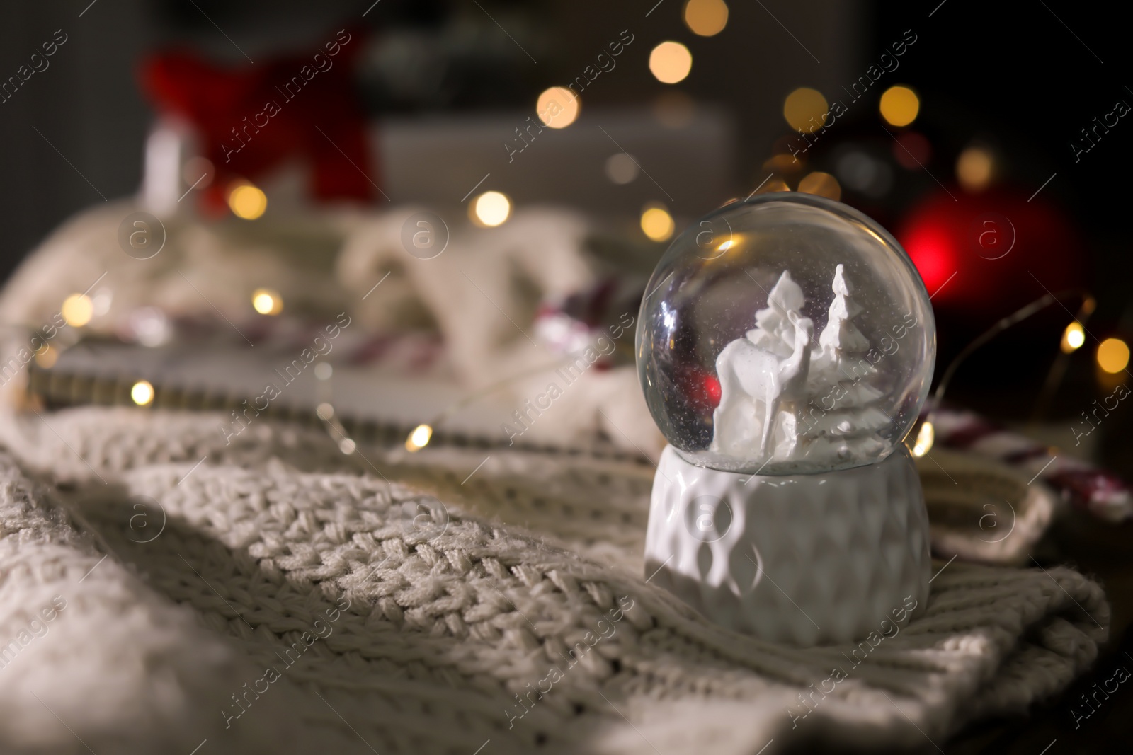 Photo of Christmas snow globe with knitting clothes on blurred background. Space for text