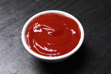 Photo of Organic ketchup in bowl on black table, closeup. Tomato sauce