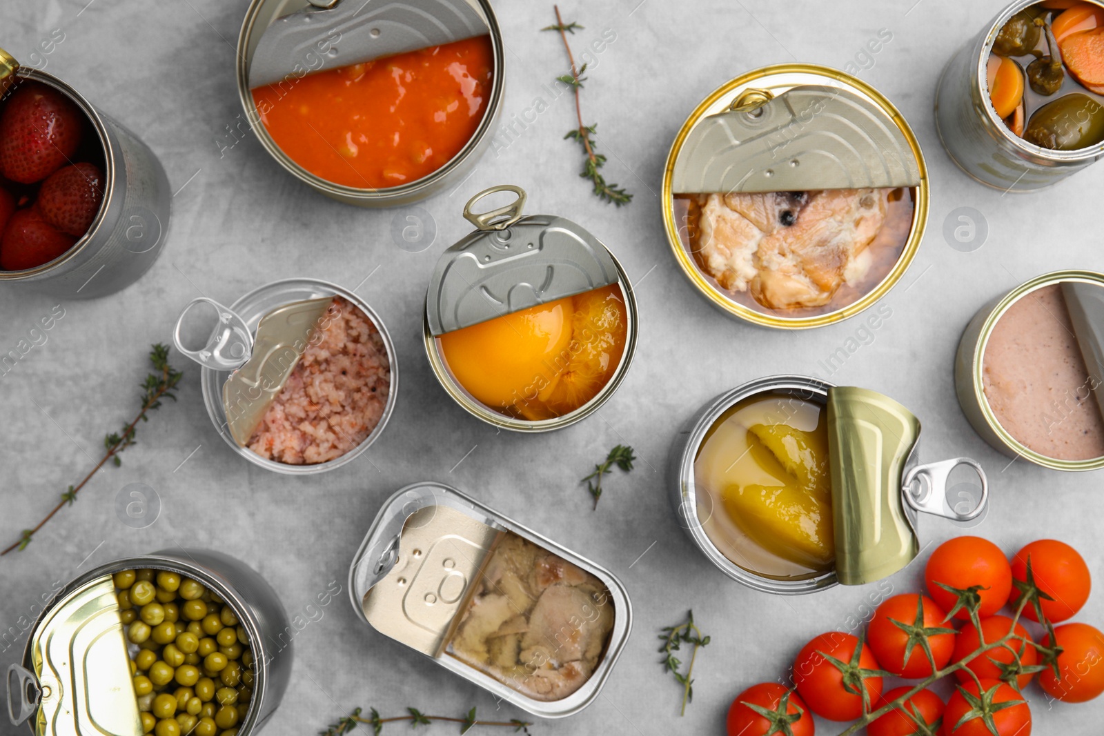 Photo of Open tin cans with different preserved products on grey table, flat lay