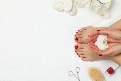 Photo of Woman with stylish red toenails after pedicure procedure and orchid flowers on white terry towel, top view. Space for text