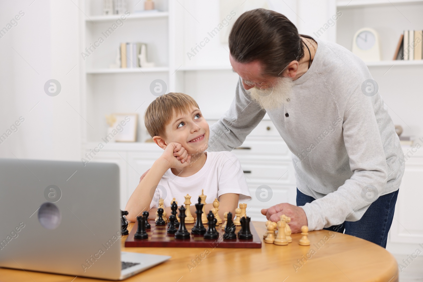 Photo of Grandfather teaching his grandson to play chess following online lesson at home